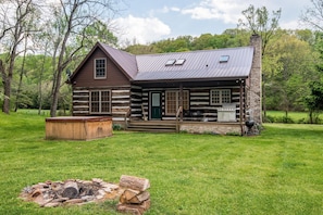 A log cabin with a porch, a fire pit, and a stone chimney.
