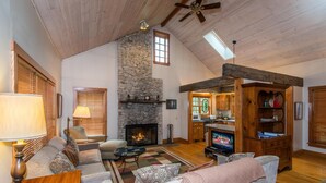 Ein gemütliches Wohnzimmer mit Kamin aus Stein, Holzbalkendecke und Fernseher.