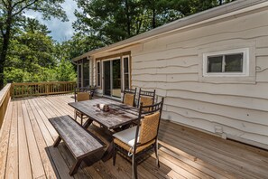 A wooden deck with a picnic table and chairs, a covered patio area, and a view of the surrounding forest.