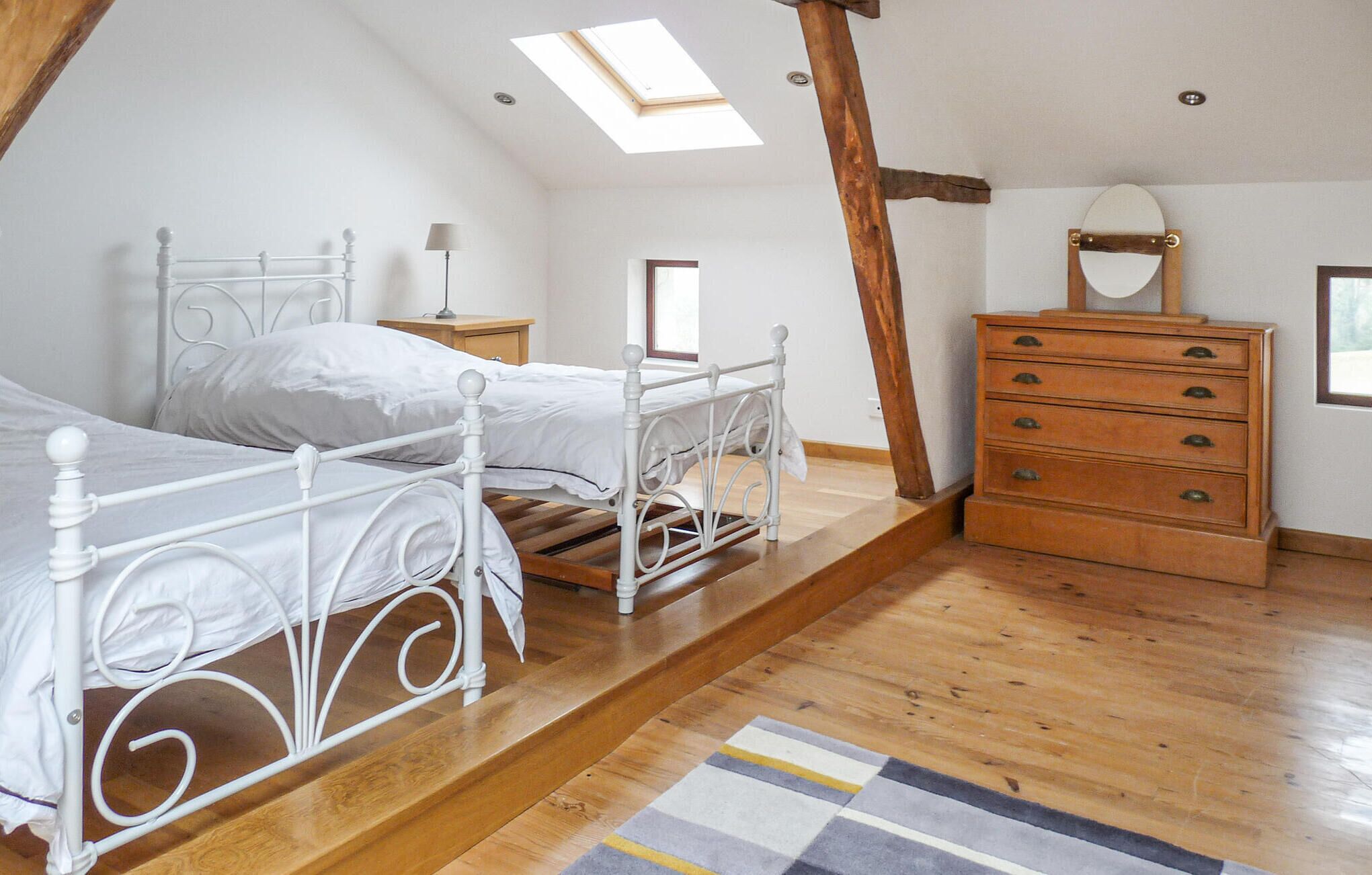A bedroom with a sloped ceiling, a skylight, a white metal bed frame, a wooden dresser, and a patterned rug.