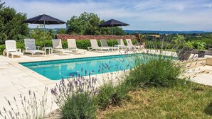Piscina rectangular con sillas de descanso blancas y sombrillas, rodeada de plantas de lavanda y vistas a colinas distantes.