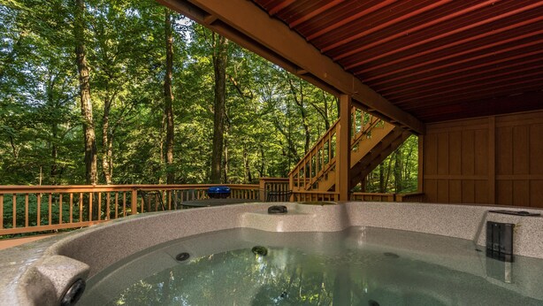 Un jacuzzi en zona boscosa con terraza de madera y escaleras que suben a un espacio cubierto.