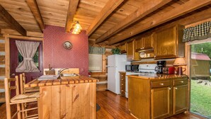 Cocina de cabaña de madera con una isla central, armarios de madera y una ventana con vistas a un jardín.