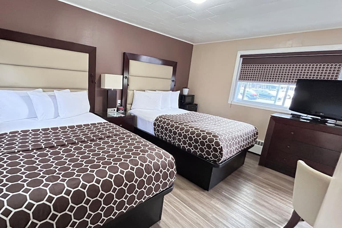 A hotel room with two beds, a television, a desk, and a window with a view of the street.