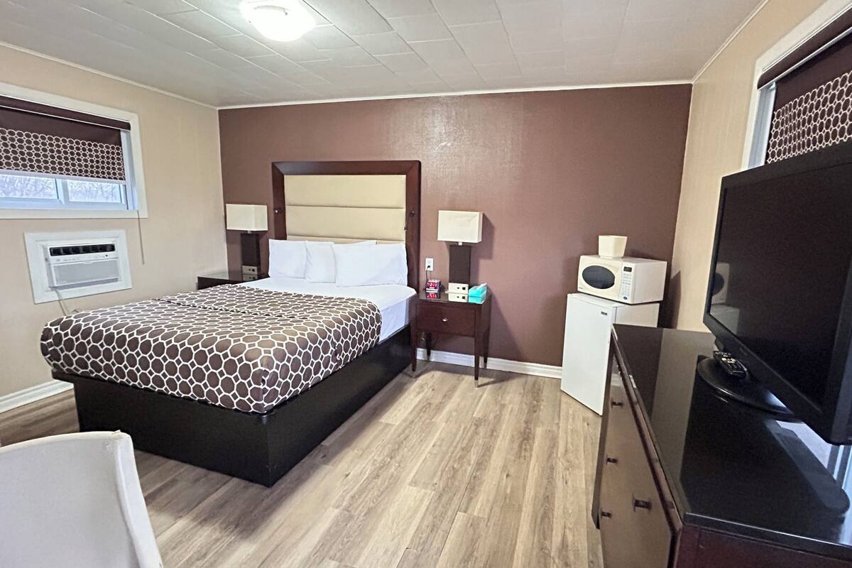 A hotel room with a bed, bedside tables, a television, a microwave, and a small refrigerator.