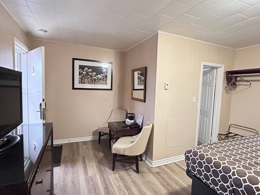 Ein Hotelzimmer mit einem Bett, einem Schreibtisch mit Stuhl, einem Fernseher und zwei gerahmten Bildern an der Wand.