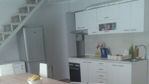 A modern kitchen with white cabinets, a dishwasher, and a sink. There's a wooden dining table with chairs and a laptop on it. - Hostel A&A (Novi Sad)