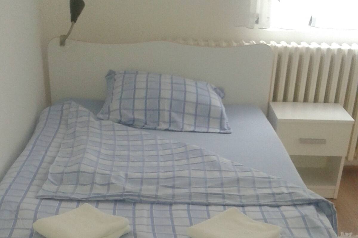 A neatly made bed with a checkered bedspread, two pillows, and a bedside table with a drawer.