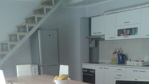 A modern kitchen with white cabinets, a dining table with chairs, and a laptop on the table. - Hostel A&A (Novi Sad)
