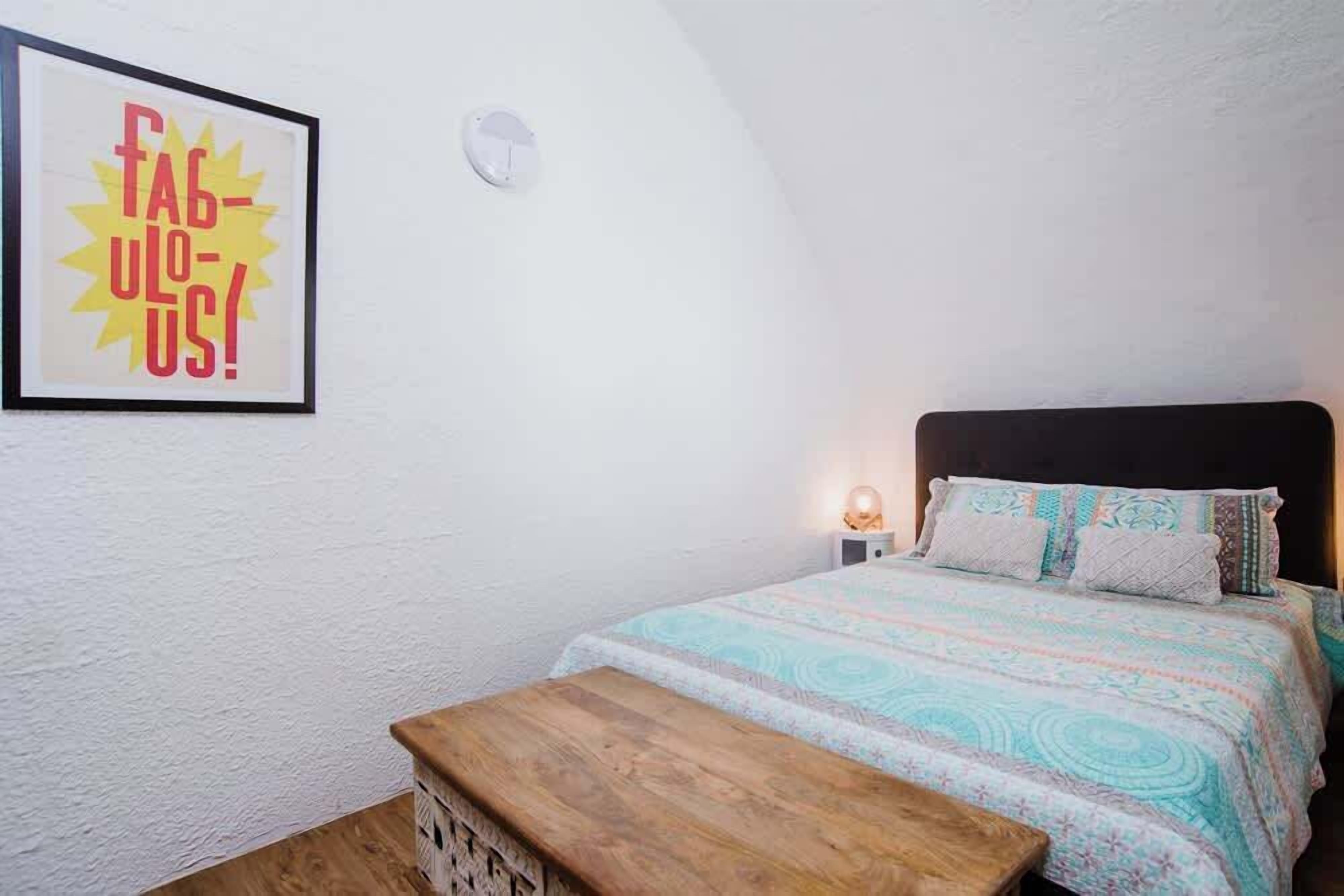 Un dormitorio con cama, mesita de noche, un reloj de pared y un cartel enmarcado.