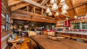 Een rustiek houten interieur met een grote eettafel, houten balken en hangende lampen.