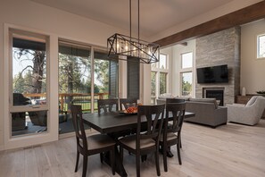 A spacious living room with a large dining table, dark wooden chairs, a fireplace, and a television mounted on the wall. - Bend Milepost 1  townhome - Mt. Bachelor, bike trails, golf  (Bend)
