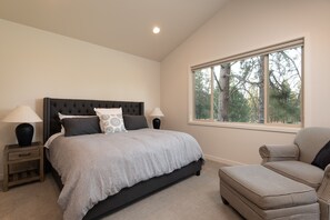 A bedroom with a large bed, two bedside tables with lamps, a window with a view of trees, and a patterned armchair. - Bend Milepost 1  townhome - Mt. Bachelor, bike trails, golf  (Bend)