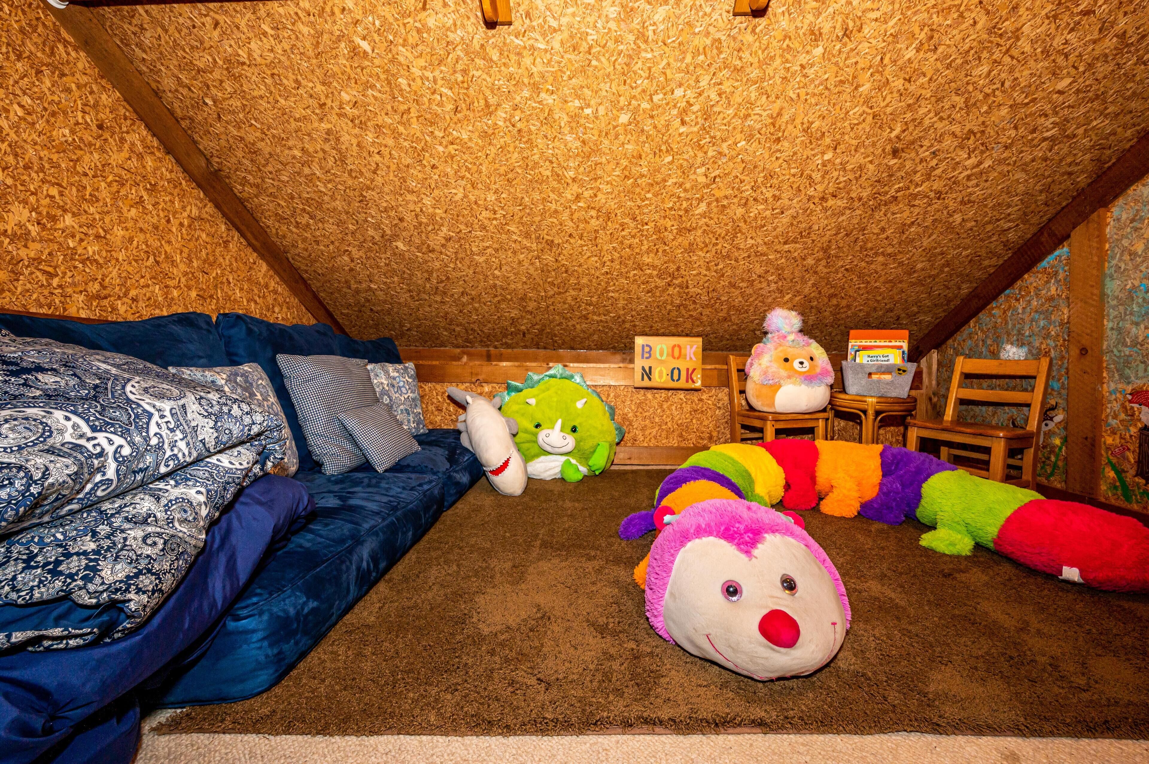 A cozy attic bedroom with a sloped ceiling, a blue sofa, a brown carpet, and various colorful stuffed animals.