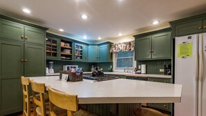 A kitchen with green cabinets, a white island, wooden chairs, and a refrigerator. - 4 BR, 2 BA Log Cabin, charming mix of old and new, close to village of Story (Nashville)