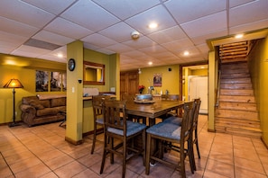 A dining area with a wooden table and chairs, a sofa, and a staircase leading to another level.