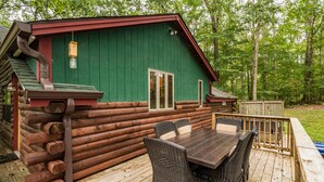 Eine Holzblockhütte mit einer Terrasse, einem Tisch und Stühlen.