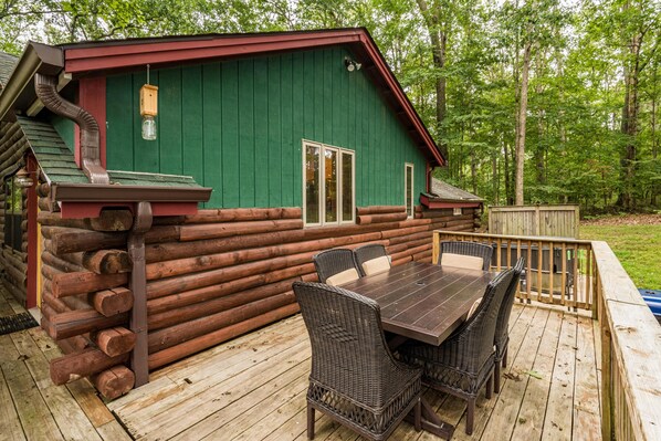 A log cabin with a deck, a table, and chairs.