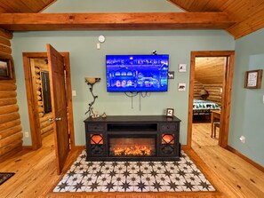 Ein Blockhaus-Interieur mit Kamin, einem an der Wand befestigten Fernseher und einem Teppich mit Sternenmuster.