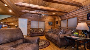 Ein rustikales Holzhaus-Interieur mit Ledersofas, einem Esstisch und einer Holzbalkendecke.