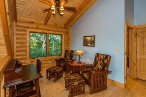 L'intérieur d'une cabane en rondins, avec une table à manger, des chaises, une lampe et une grande fenêtre donnant sur la forêt.