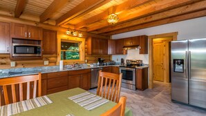 A modern kitchen with wooden cabinets, stainless steel appliances, and a dining area with a table and chairs. - View Cabin w/ Hot Tub, Pond & Pool Table | Secluded Retreat 3BR, 2BA (Nashville)