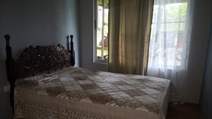 Ein Schlafzimmer mit einem hölzernen Kopfteil, einer gesteppten Bettdecke und einem Fenster mit Vorhängen.