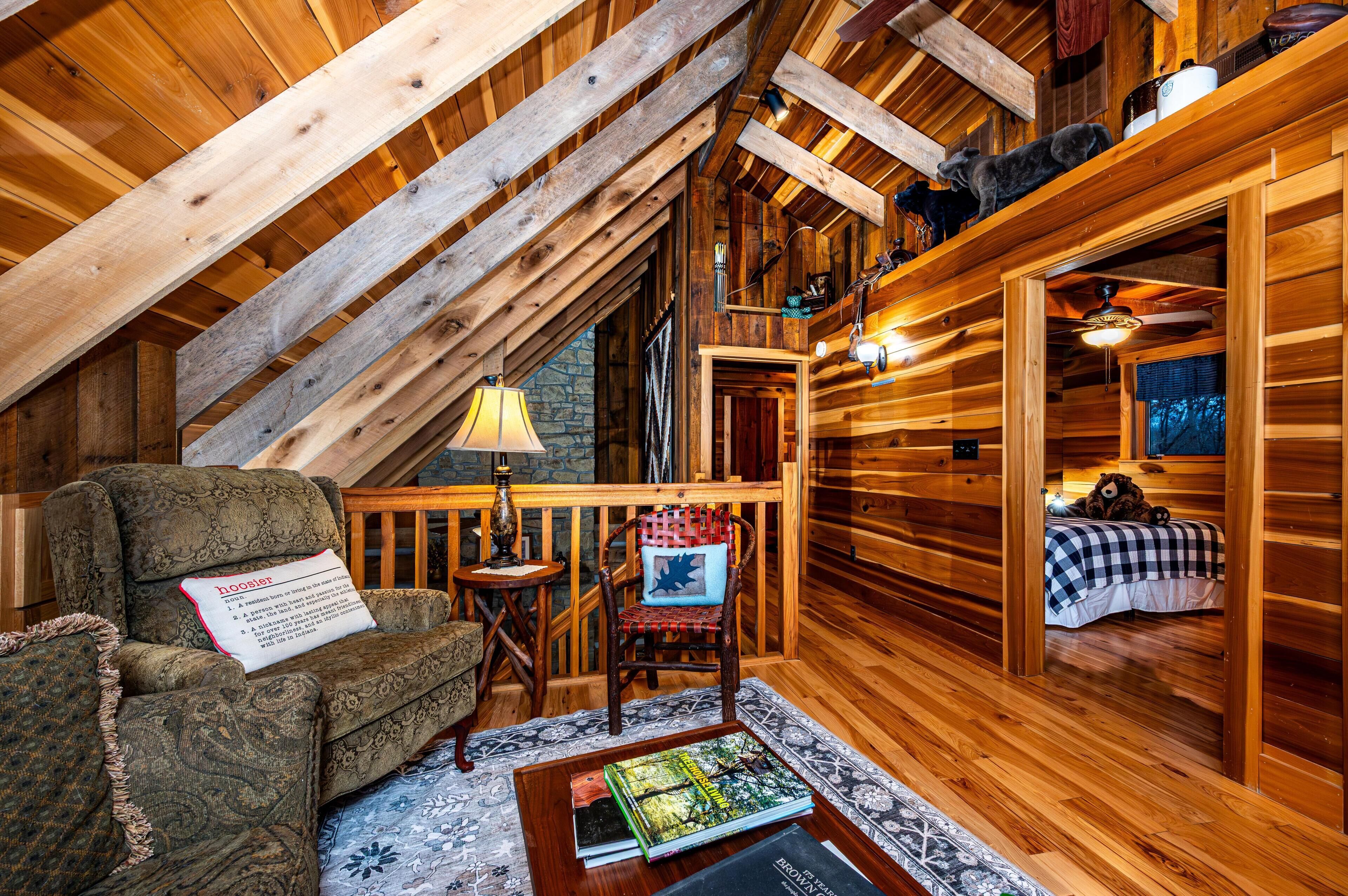 Ein gemütliches Blockhaus-Interieur mit Holzbalkendecke, Kamin, einer komfortablen Sitzecke und einem Bett.