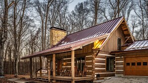 Une cabane en rondins avec un porche, un garage et une cheminée.