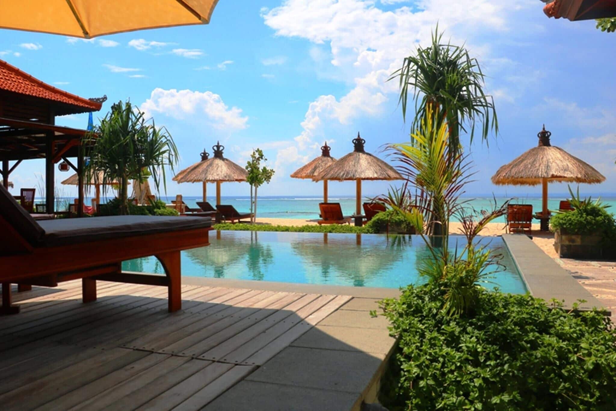 A poolside area with lounge chairs, thatched umbrellas, and a view of the ocean.