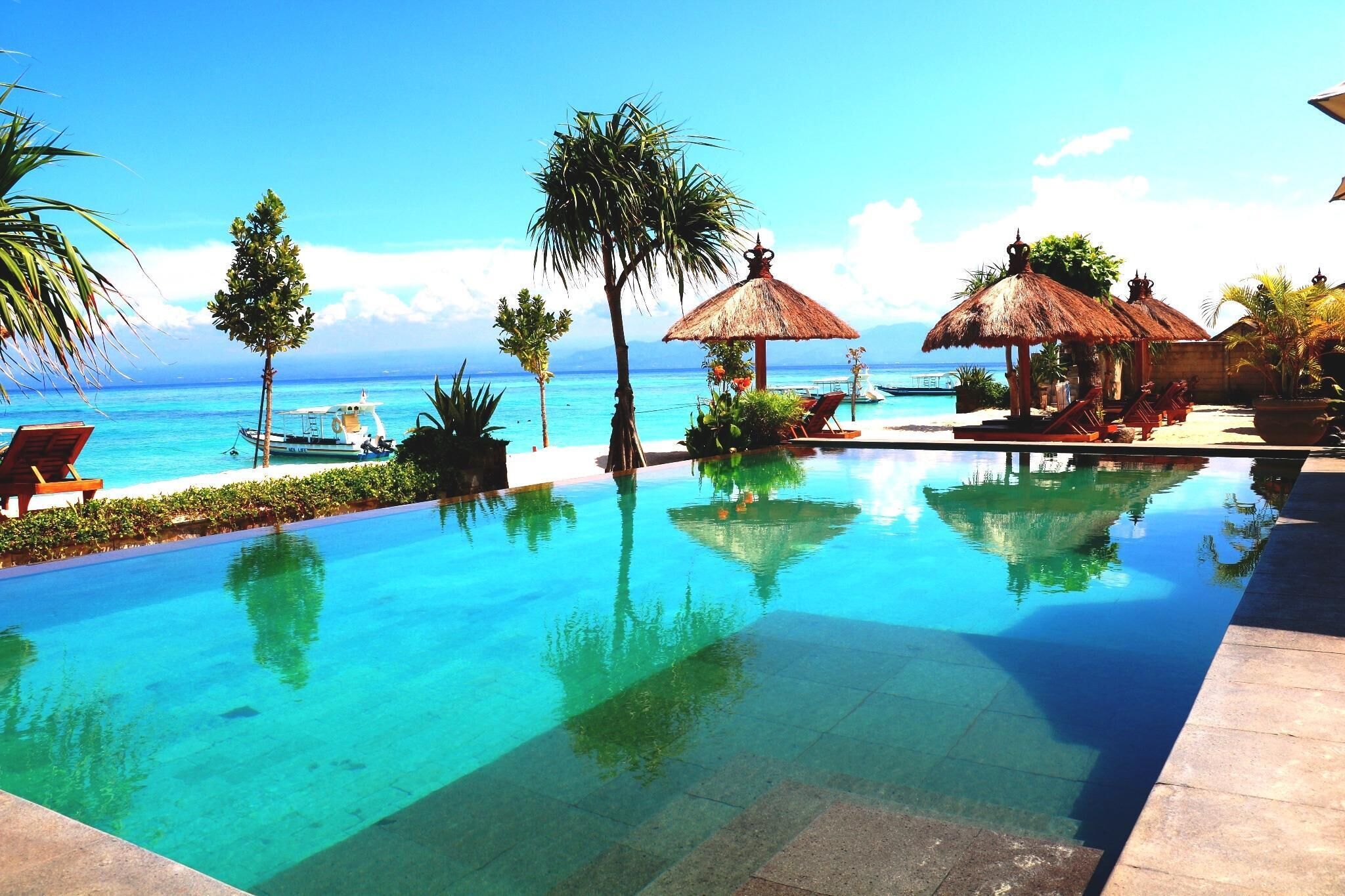 A clear pool with lounge chairs and umbrellas, a boat, and a view of the ocean.