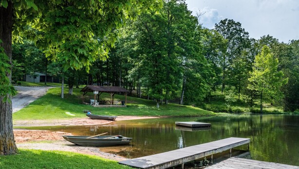 Eine friedliche Seenlandschaft mit Holzsteg, einem kleinen Boot und einem überdachten Pavillon.
