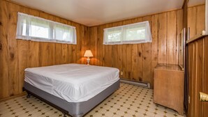 Ein Zimmer mit Holzwänden, einem Bett, einem Nachttisch und einem Fenster mit Lampe.