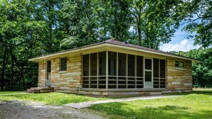 Ein Steinhaus mit Veranda und großen Fenstern, umgeben von Bäumen.