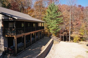 A two-story wooden cabin with a balcony, surrounded by autumn foliage.