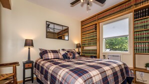 Ein Schlafzimmer mit einem großen Bett, einem Fenster mit Jalousien, einem Bücherregal und einem Spiegel an der Wand.