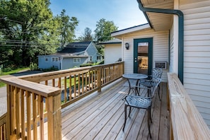 A wooden deck with a table and chairs, a door, and a small building in the background.