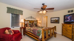A bedroom with a wooden bed, a red couch, a ceiling fan, a television, and a dresser. - Romantic Cottage for Two | Hot Tub, Fireplace & Near Nashville 1 BR, 1BA (Morgantown)