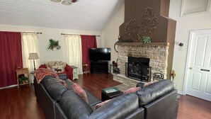 A living room with a sectional sofa, a fireplace, a ceiling fan, and a television. - Romantic Cottage for Two | Hot Tub, Fireplace & Near Nashville 1 BR, 1BA (Morgantown)
