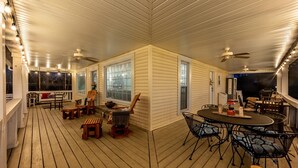 A covered deck with wooden flooring, outdoor seating, and ceiling fans.