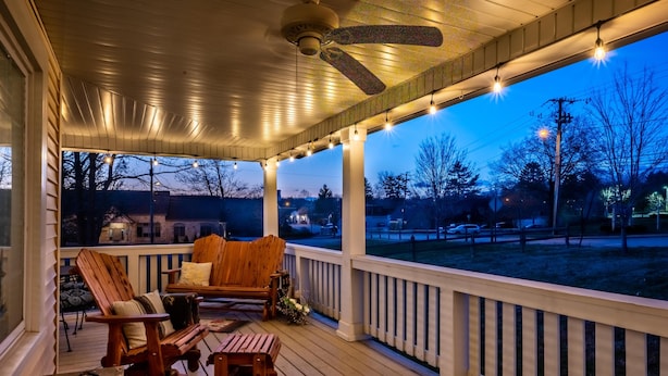 A wooden deck with a ceiling fan, string lights, and two wooden chairs.