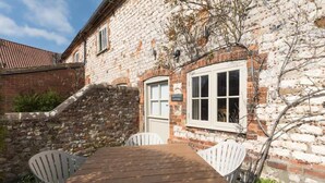A stone building with a wooden table and white chairs, a small window, and a door. - Stunning Driftwood Cottage at Holme-next-the-sea (Hunstanton)