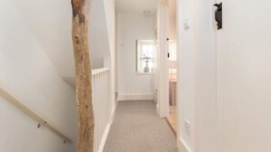 A narrow hallway with a wooden beam on the left, white walls, and a carpeted floor. - Stunning Driftwood Cottage at Holme-next-the-sea (Hunstanton)