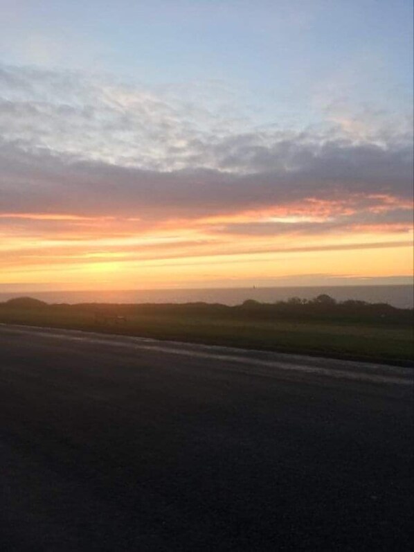 A sunset over a flat landscape with a road in the foreground.