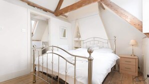A bedroom with a metal bed frame, wooden floor, and a sloped ceiling with exposed beams. - Stunning Driftwood Cottage at Holme-next-the-sea (Hunstanton)