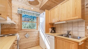 Cozinha de cabana de madeira, com fogão, pia e janela com vista para o verde.