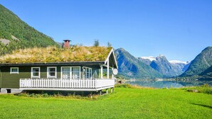 Uma casa com varanda, rodeada por um campo gramado e montanhas.