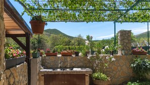 Un espace cuisine extérieur doté de murs en pierre, d’un banc en bois et de différents pots de plantes.
