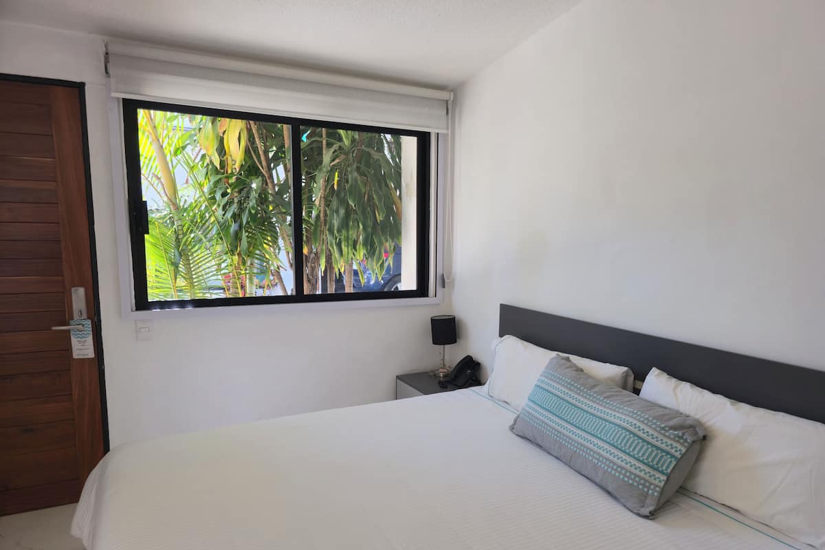 Une chambre à coucher avec un grand lit, une table de chevet, un téléphone et une fenêtre donnant sur des palmiers.