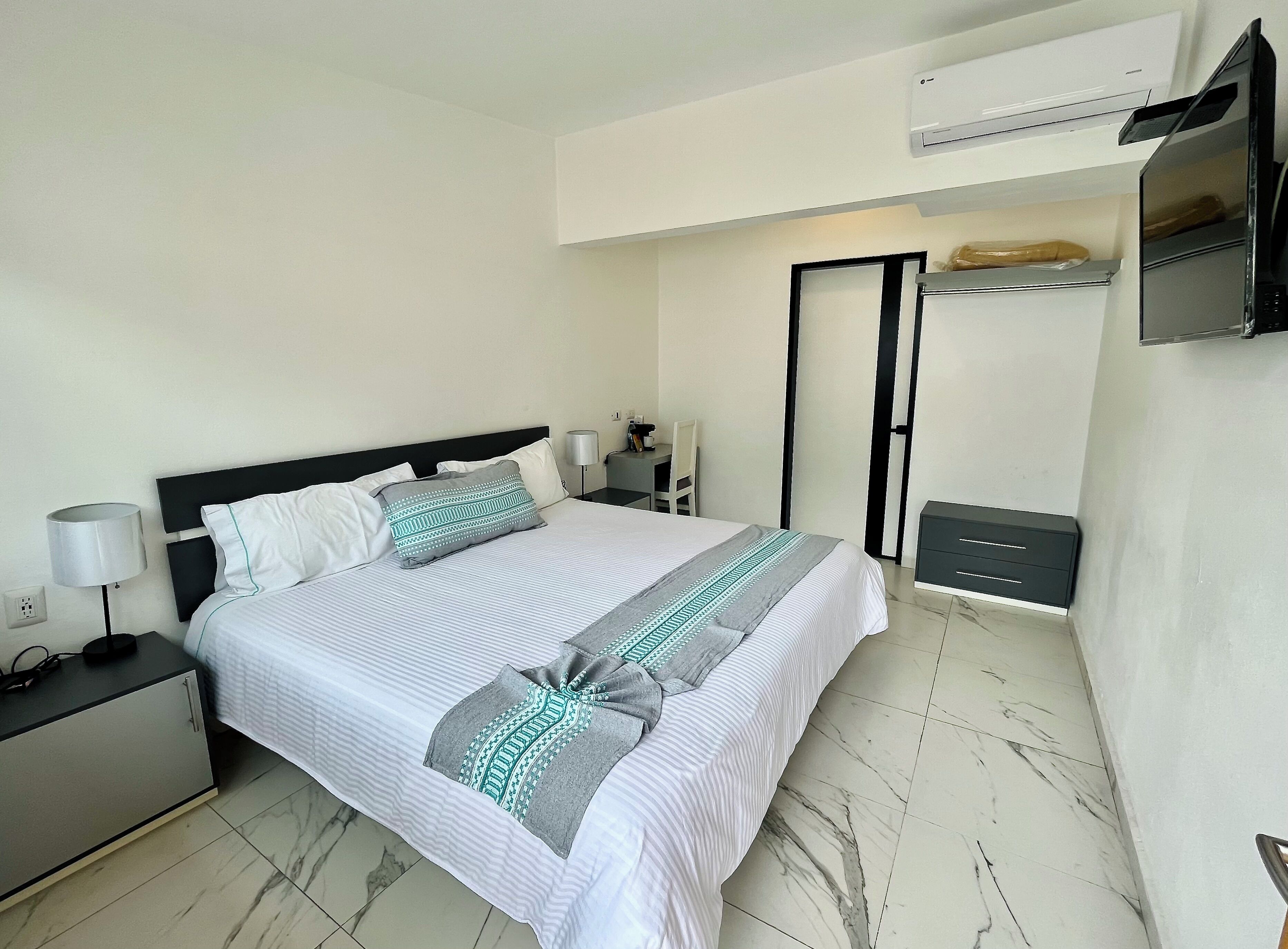 Een keurig opgemaakt slaapkamer met een bed, nachtkastjes, een bureau, een airconditioning en een garderobe.